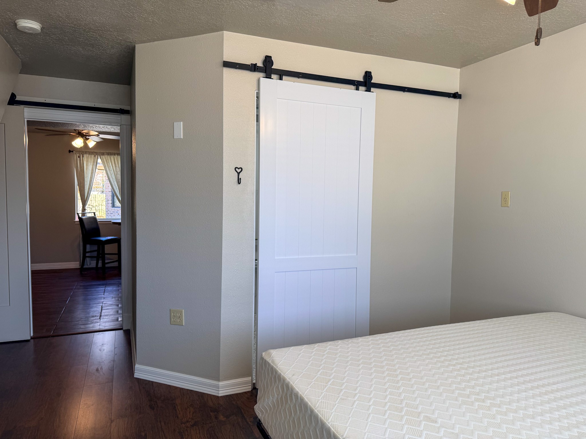 24527 Appian Ridge, Unit B Porter, TX 77365 - Photo 7 of 10 This bedroom features a sliding barn door, hardwood flooring, and neutral walls. The room is adjacent to a dining area with natural light and a ceiling fan.
