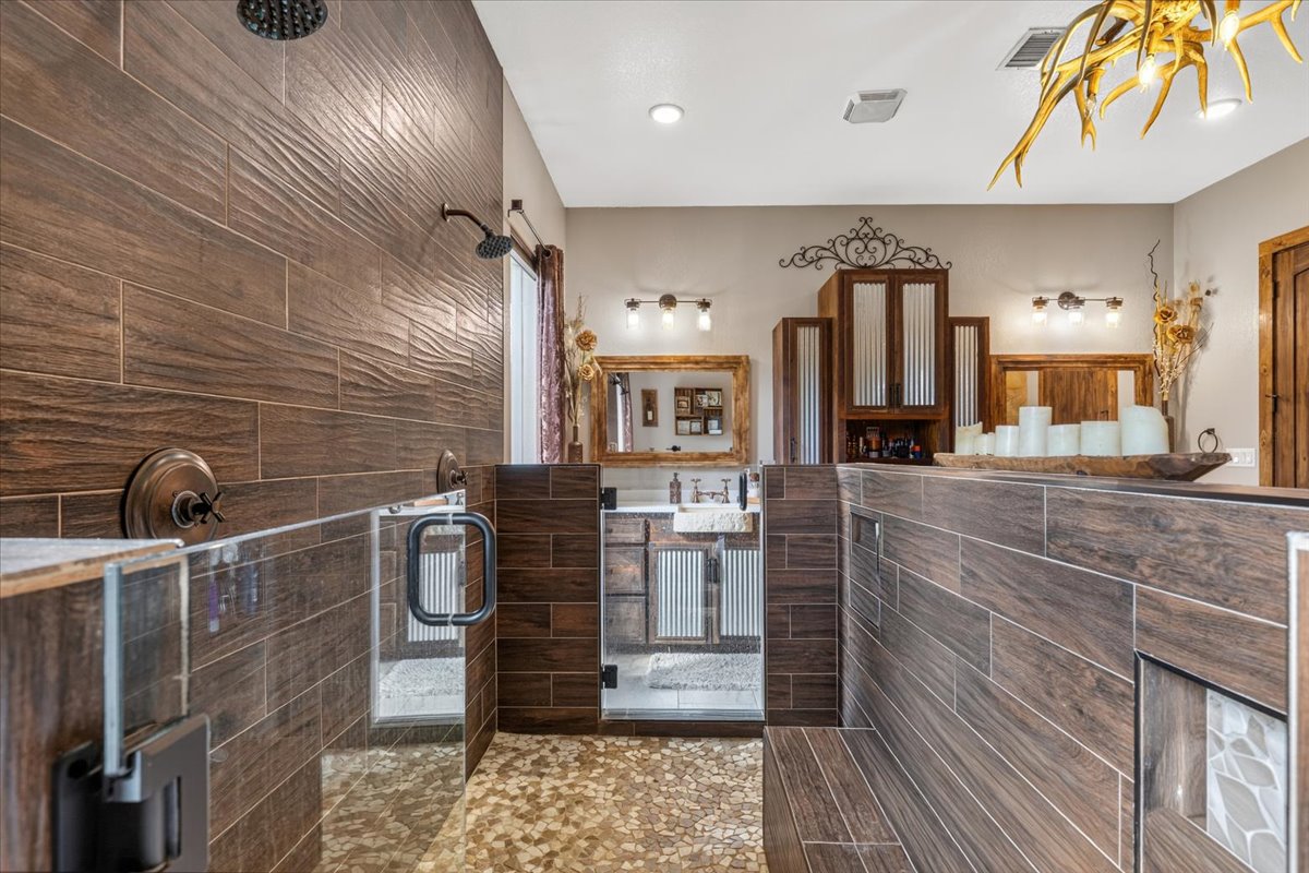 175 Wilson Road Elgin, TX 78621 - Photo 20 of 40 And here’s a look inside that unique walk-in shower! You’ve got dual shower heads mounted against deep wood-look tile, pebble stone flooring underfoot for a spa-like texture, built-in recessed niches for products, and a long tiled bench seat. Glass doors on either end complete the high-end, seamless design.