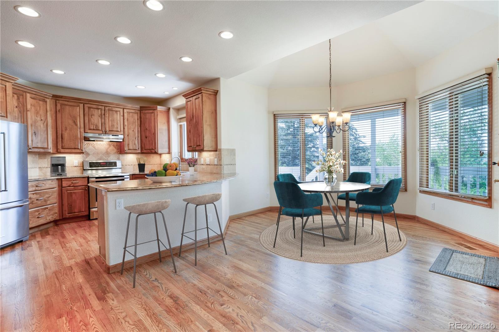 3756 West 100th Avenue Westminster, CO 80031 - Photo 5 of 45 a kitchen with kitchen island granite countertop a stove a sink a refrigerator a dining table and chairs with wooden floor