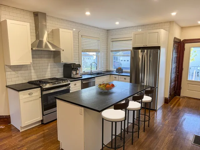 a kitchen with stainless steel appliances granite countertop a stove a refrigerator a sink a dining table and chairs with wooden floor