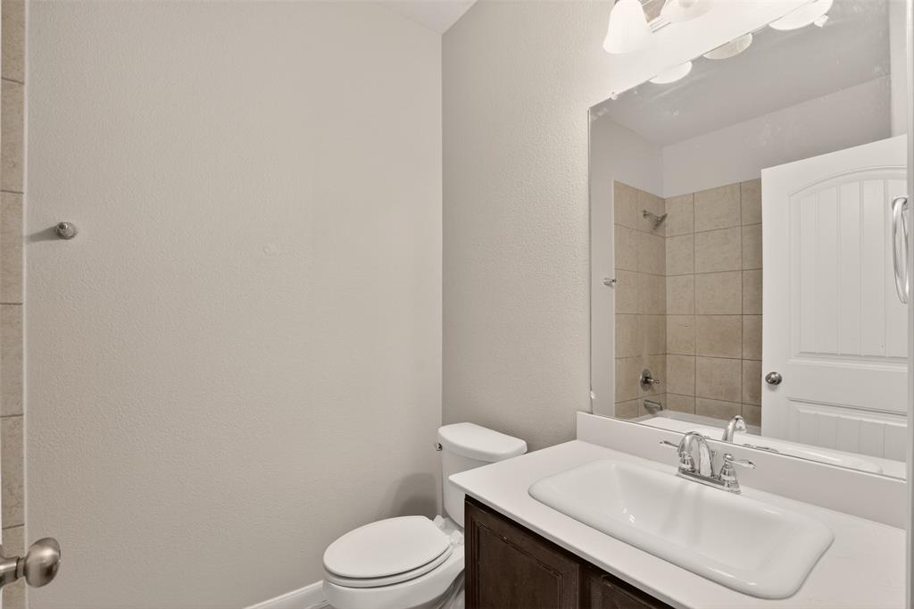9105 Switchgrass Lane Forney, TX 75126 - Photo 6 of 20 Bathroom featuring a white elongated toilet, a vanity with a dark wood-finish cabinet, a white countertop, an integrated sink, and a large wall mirror
