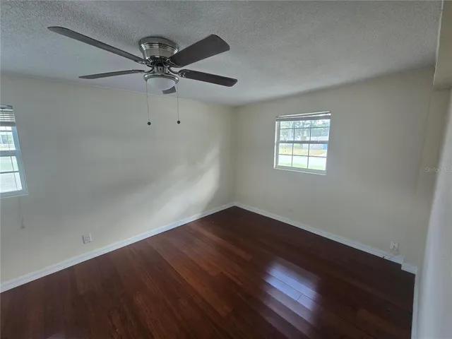 an empty room with wooden floor fan and windows