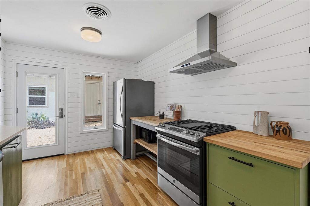 900 Stark Street Austin, TX 78756 - Photo 7 of 25 A well-equipped kitchen features a gas range, a stainless steel refrigerator, and natural wood flooring, with a glass-paneled door leading outdoors.