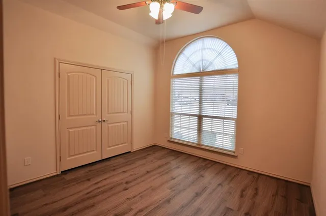 an empty room with wooden floor chandelier fan and windows