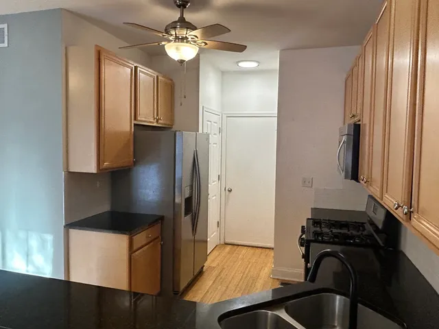 a kitchen with stainless steel appliances granite countertop a refrigerator a sink dishwasher a stove and a dining table with wooden floor