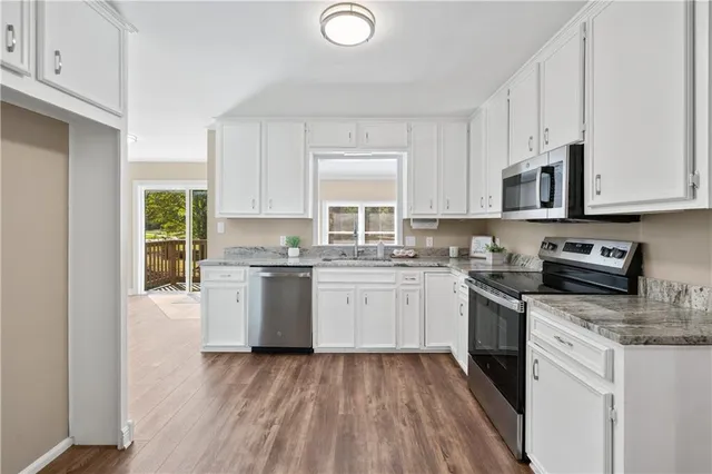 a kitchen with granite countertop white cabinets a sink a window and stainless steel appliances