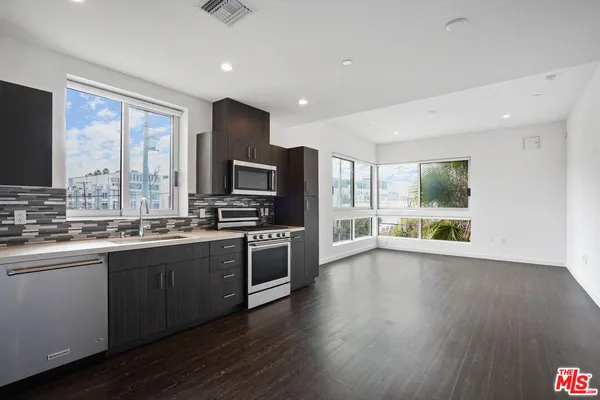 a large kitchen with stainless steel appliances granite countertop a stove a sink dishwasher a microwave oven and a refrigerator with wooden floor