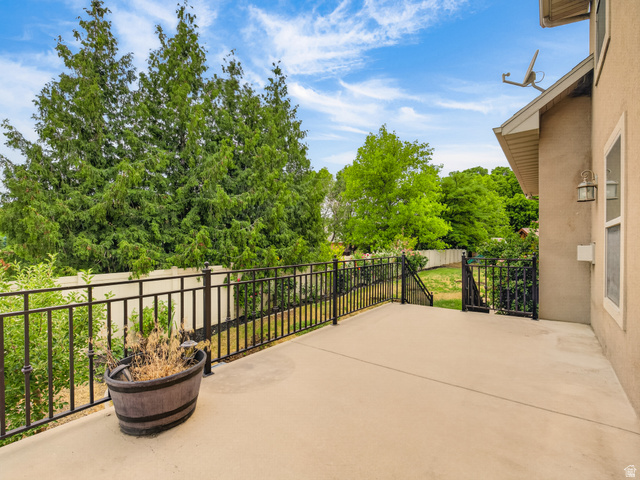 1279 West 1500th Street North Mapleton, UT 84664 - Photo 67 of 83 Expansive concrete patio with wrought iron railing, exterior wall sconce, and mature perimeter trees