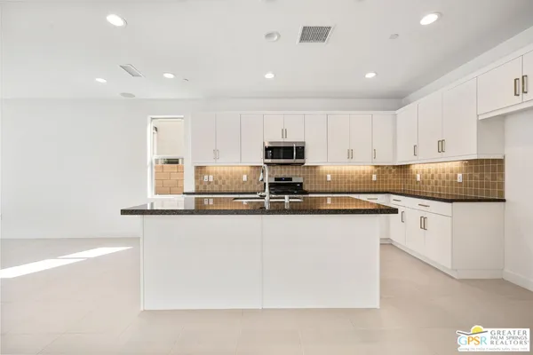 a kitchen with kitchen island granite countertop a sink a stove a microwave a counter top space and cabinets