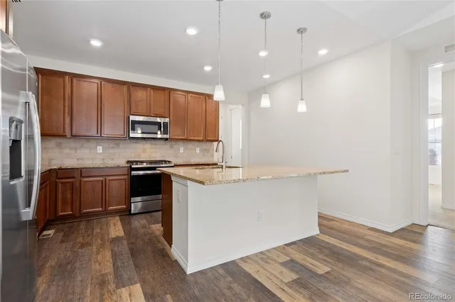 a kitchen with kitchen island granite countertop wooden floors appliances and cabinets
