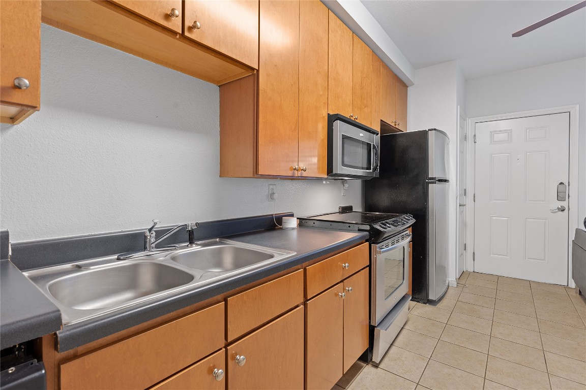 2515 Pearl Street, Unit 102 Austin, TX 78705 - Photo 22 of 30 Kitchen with stainless steel appliances, dark countertops, light tile patterned floors, and brown cabinetry