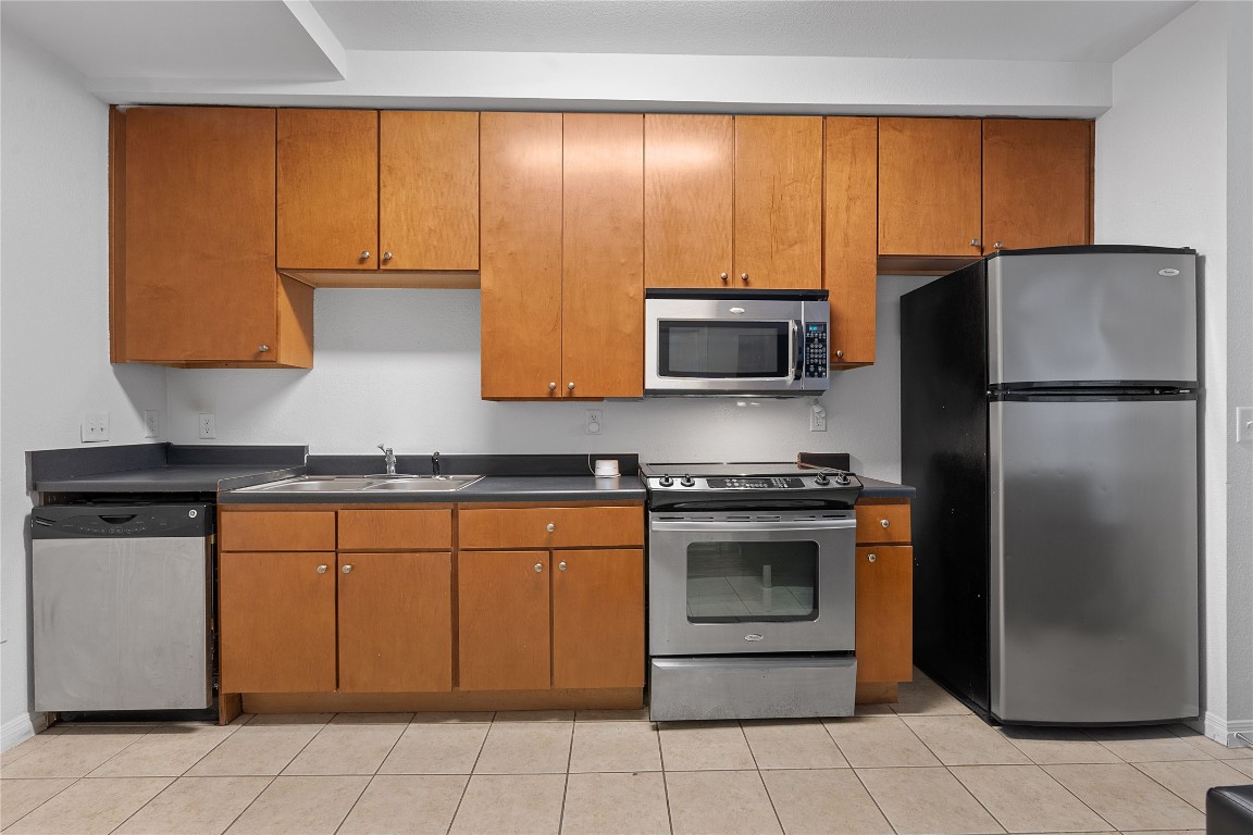 2515 Pearl Street, Unit 102 Austin, TX 78705 - Photo 30 of 30 Kitchen featuring stainless steel appliances, dark countertops, and brown cabinets