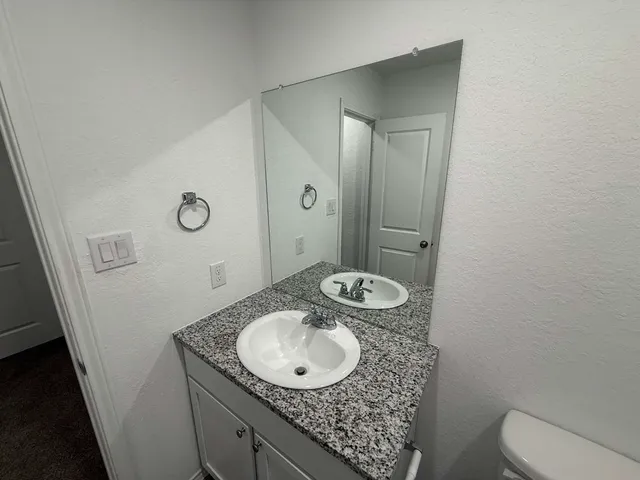 a bathroom with a granite countertop sink a mirror and a toilet