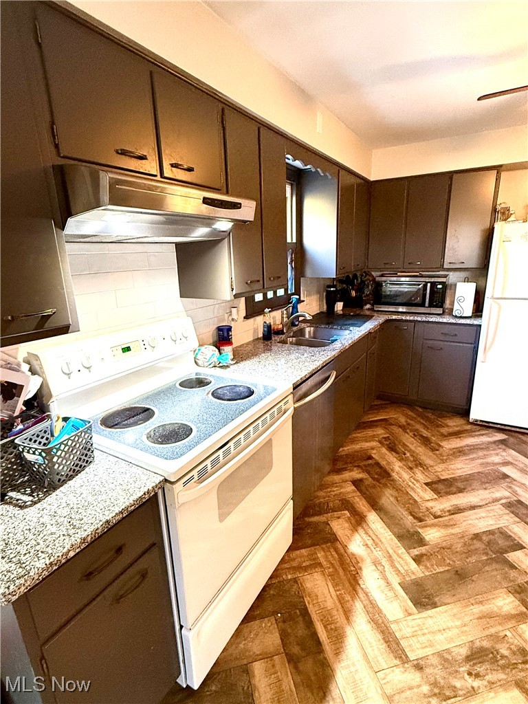 Kitchen with backsplash, dark parquet flooring, sink, light stone countertops, and white appliances