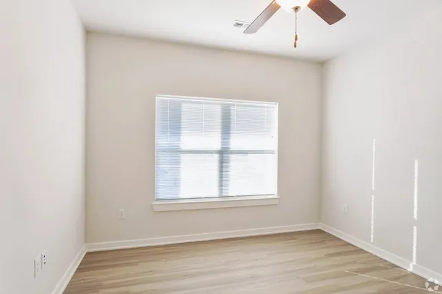an empty room with wooden floor fan and windows