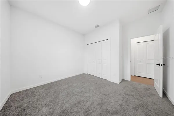 a view of an empty room with wooden floor and a kitchen