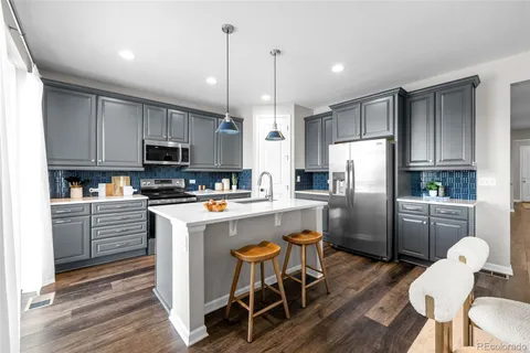 a kitchen with stainless steel appliances a refrigerator a stove a sink dishwasher a dining table and chairs with wooden floor