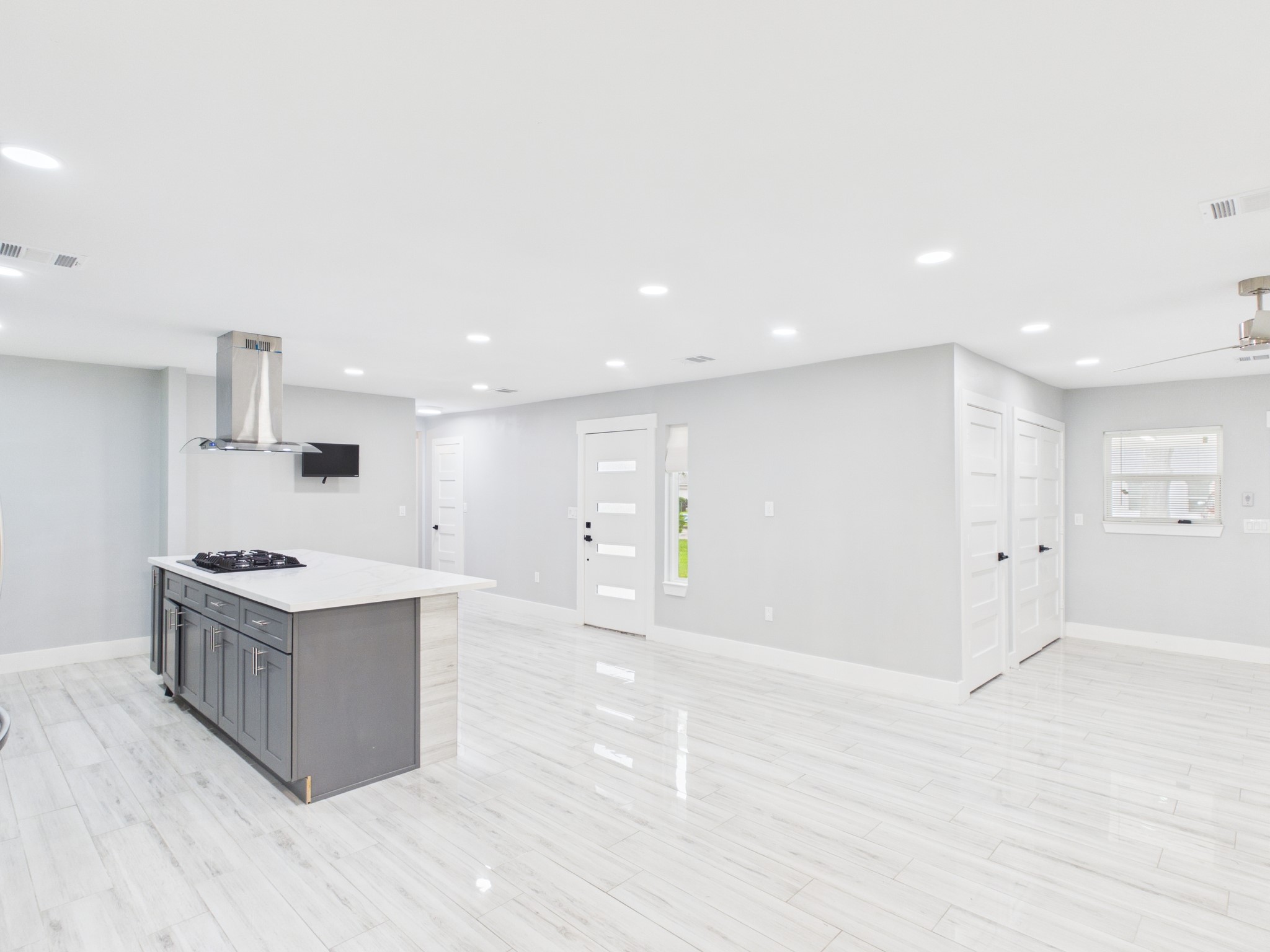 4927 Kelso Street Houston, TX 77021 - Photo 2 of 45 This photo shows a spacious, open-concept kitchen and living area with modern finishes. It features sleek white walls, recessed lighting, glossy tile flooring, and an island with a cooktop and stainless steel hood. The space is bright and inviting, perfect for entertaining.