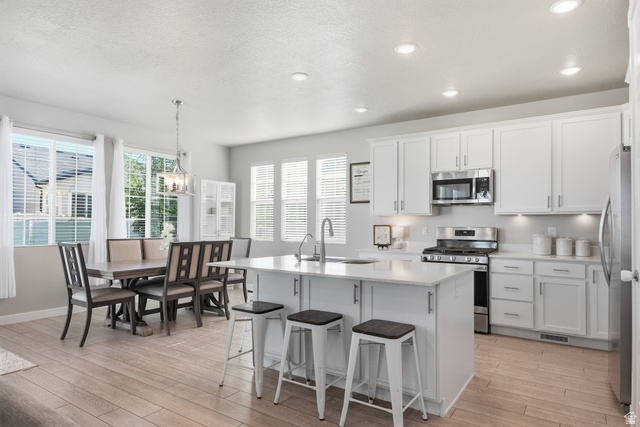 3244 West 1670th Street North Provo, UT 84601 - Photo 11 of 56 Open-concept kitchen and dining area featuring light-finish flooring, white cabinetry, a kitchen island with seating, stainless steel appliances, and abundant natural light from multiple windows
