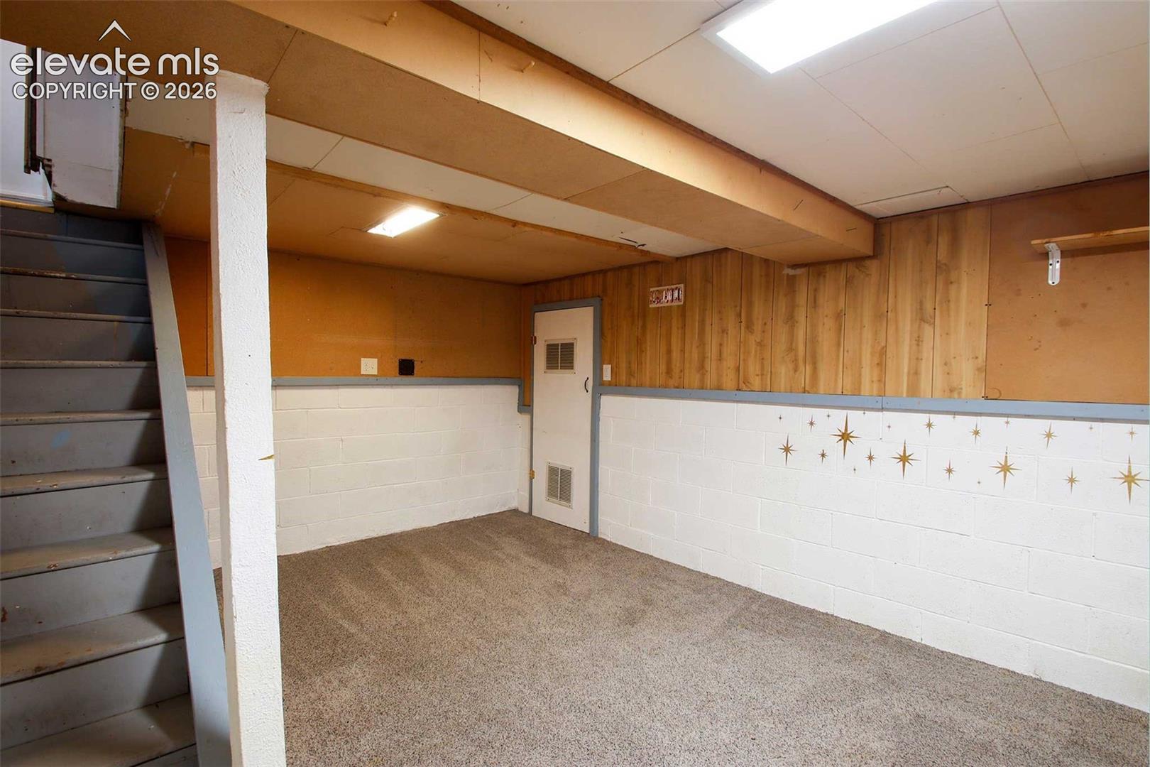 702 Erie Road Colorado Springs, CO 80910 - Photo 16 of 19 Carpeted floor, painted cinder block walls, wood paneling, and exposed ceiling beams