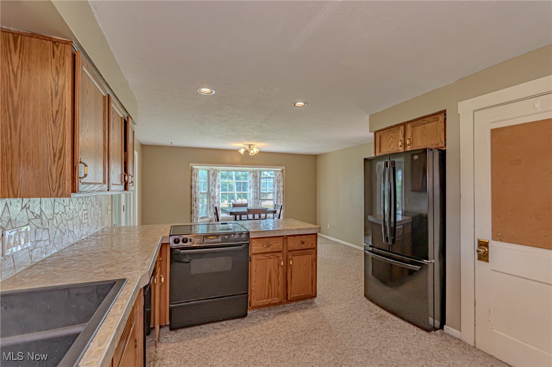 749 Hartman Road Wadsworth, OH 44281 - Photo 30 of 49 Kitchen featuring tasteful backsplash, sink, black appliances, kitchen peninsula, and light carpet