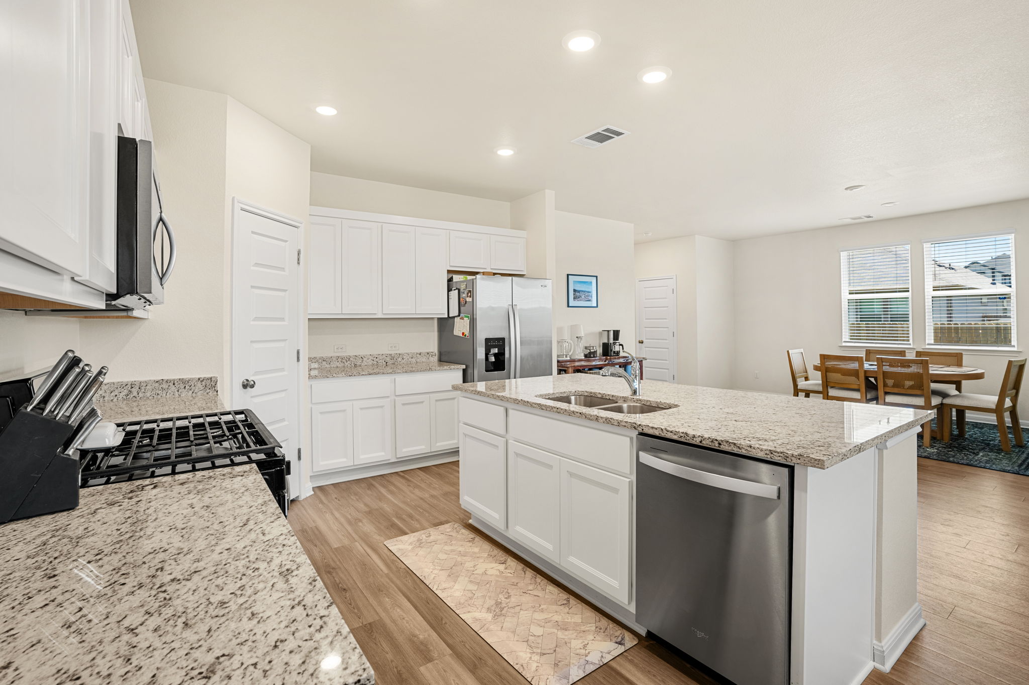 148 Hidalgo Lane Elgin, TX 78621 - Photo 9 of 38 A contemporary kitchen features bright white cabinetry and granite countertops, complemented by recessed lighting and durable wood flooring.