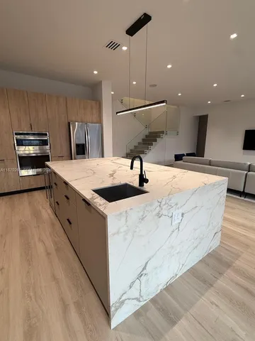 a large kitchen with stainless steel appliances kitchen island a large counter top a sink a stove and a refrigerator