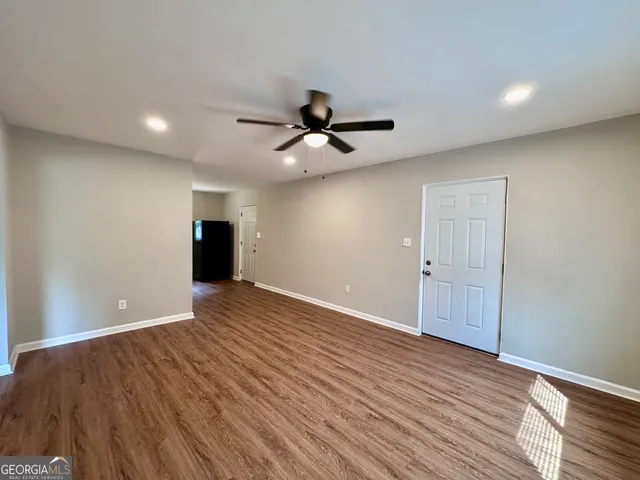 a view of an empty room with wooden floor and a ceiling fan