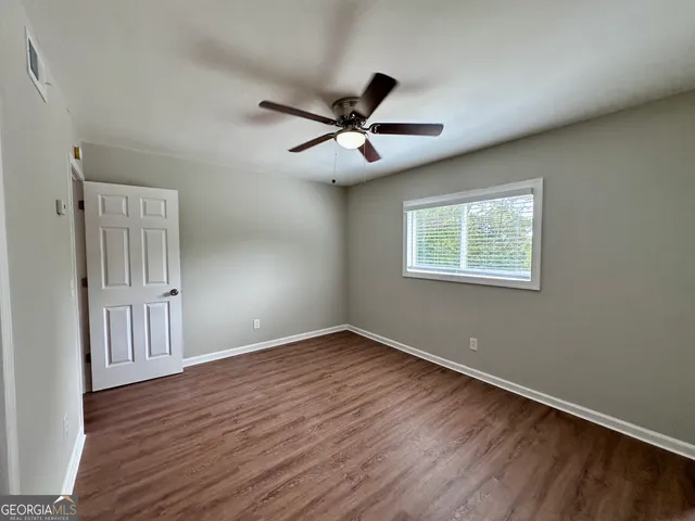 an empty room with wooden floor ceiling fan and windows