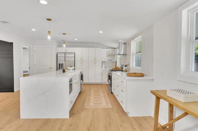 a large white kitchen with wooden floor and stainless steel appliances