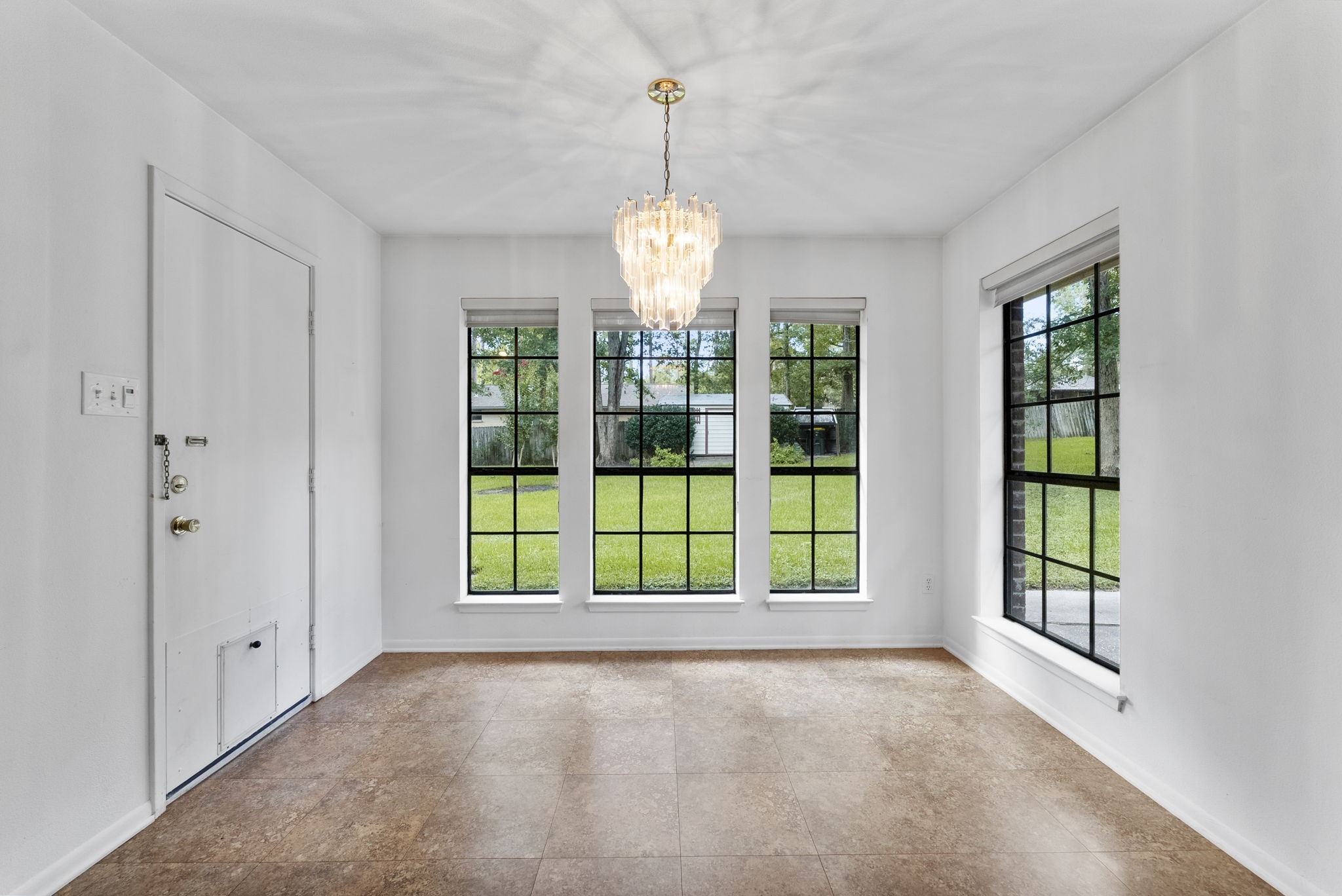 202 Sunset Boulevard Conroe, TX 77303 - Photo 22 of 50 Enjoy your mornings in this bright and inviting breakfast area, featuring large windows that offer serene views of the lush backyard, complemented by elegant tile flooring and a stunning chandelier.