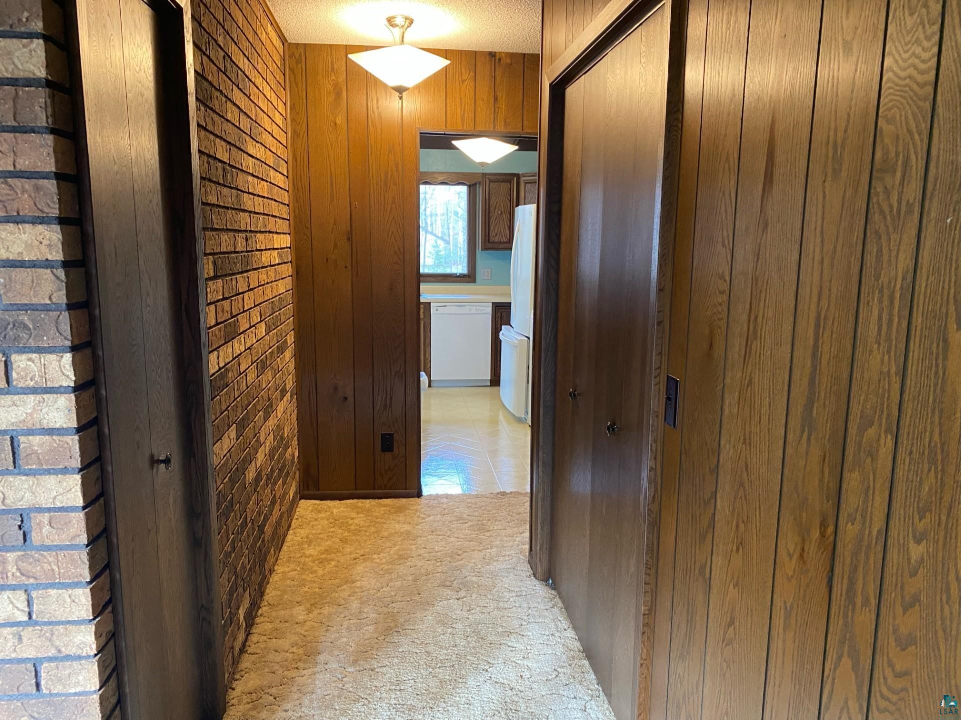 11316 East Timber Ridge Drive Lake Nebagamon, WI 54849 - Photo 14 of 27 Hallway featuring wood walls, a textured ceiling, and light carpet