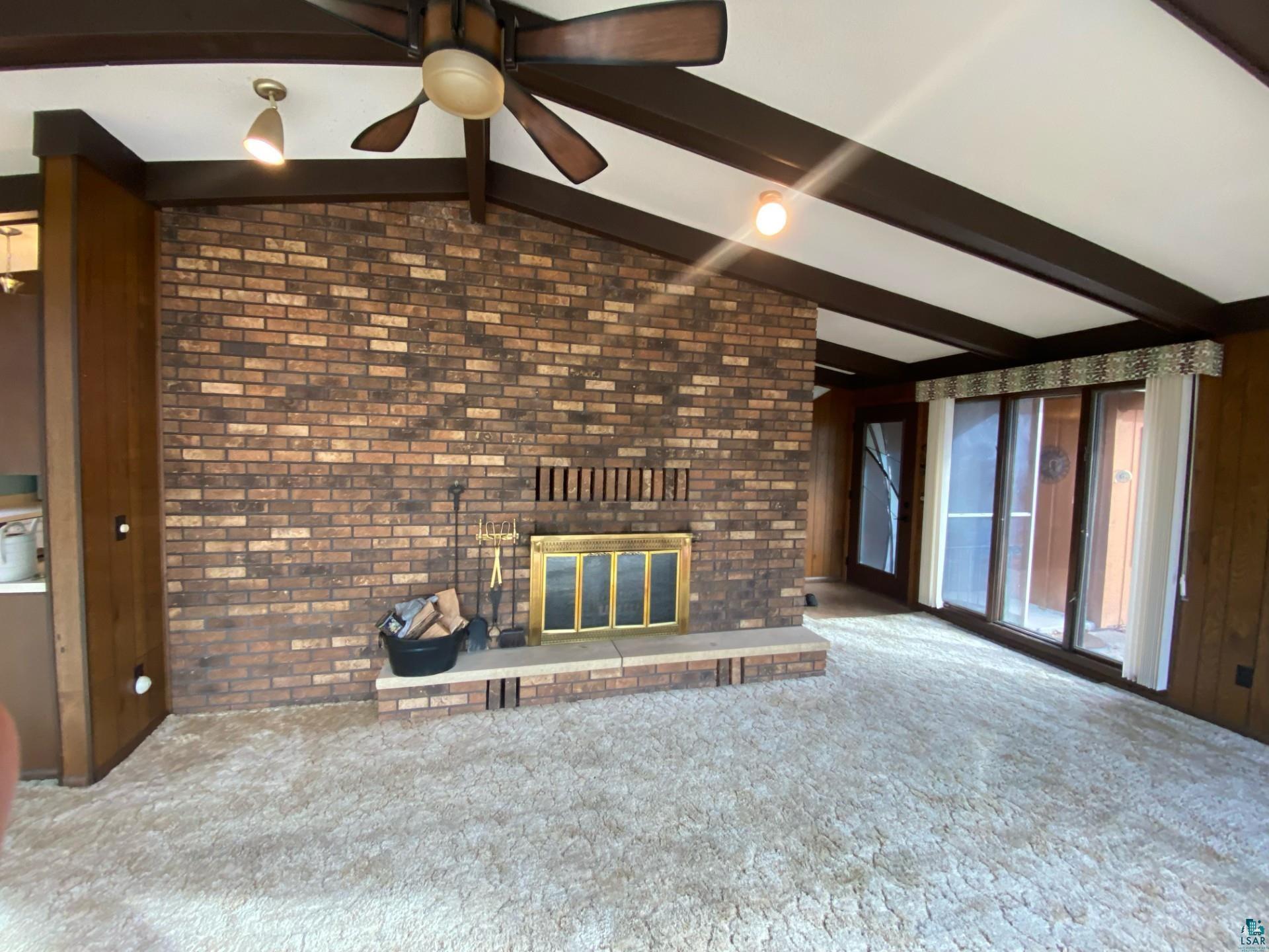 11316 East Timber Ridge Drive Lake Nebagamon, WI 54849 - Photo 8 of 27 Unfurnished living room with vaulted ceiling with beams, carpet floors, a brick fireplace, ceiling fan, and brick wall