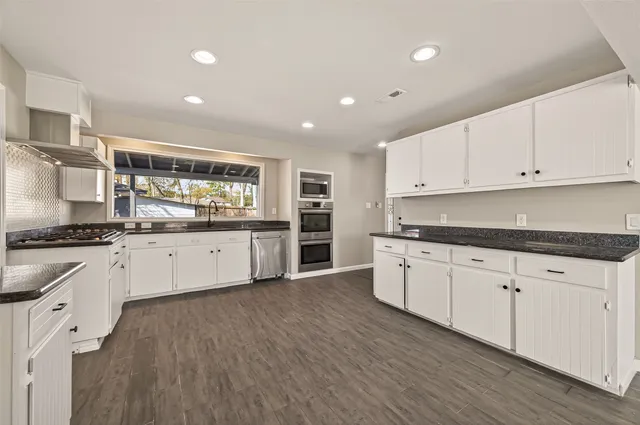 a large white kitchen with stainless steel appliances granite countertop a stove a sink dishwasher and white cabinets with wooden floor