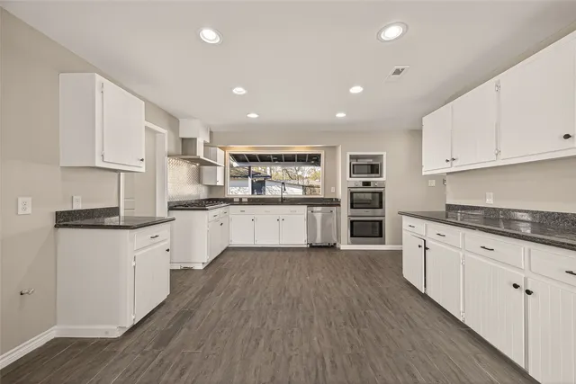 a large kitchen with stainless steel appliances granite countertop a stove top oven a sink dishwasher and a refrigerator with wooden floor