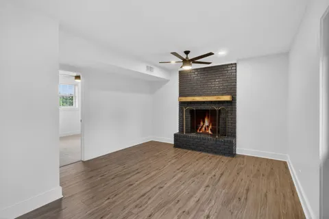 an empty room with wooden floor ceiling fan and windows