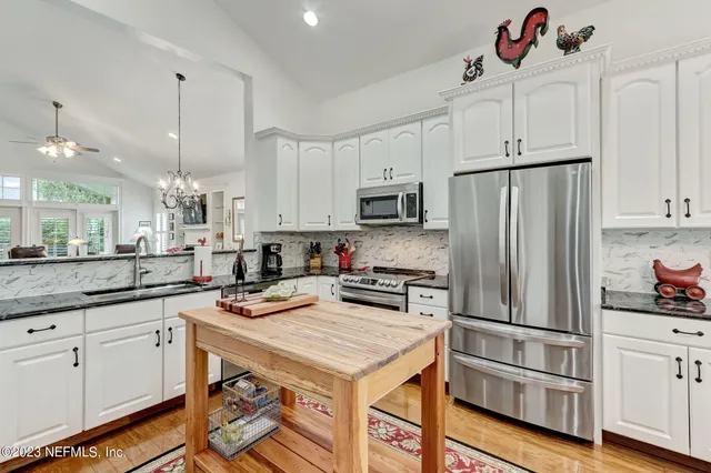 a kitchen with stainless steel appliances granite countertop a dining table chairs and a refrigerator a sink with wooden floor