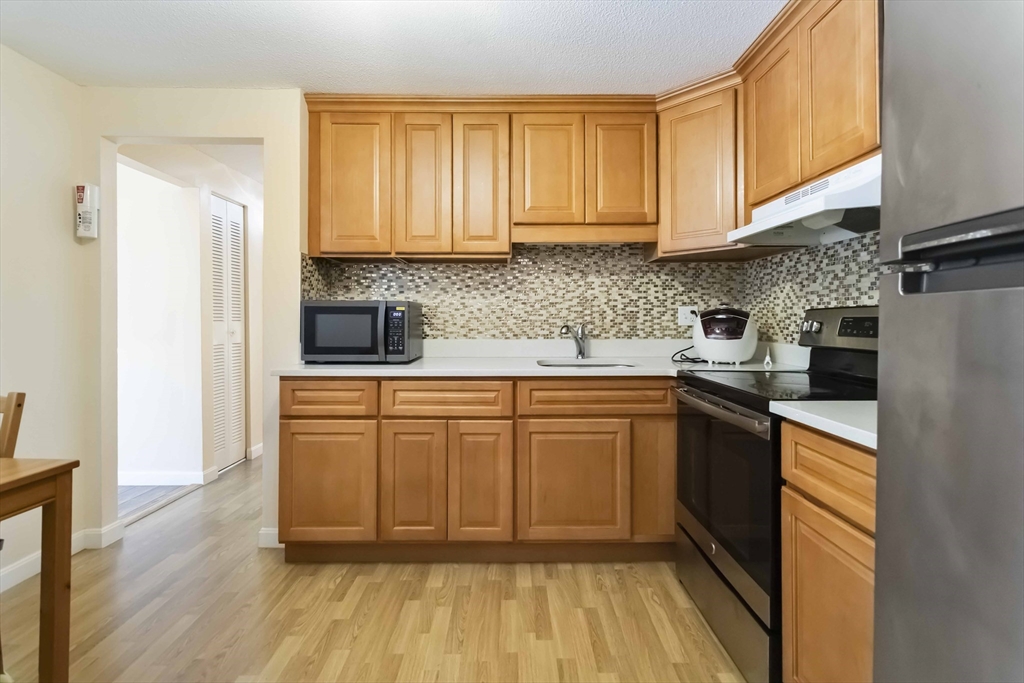 388 Great Road, Unit B14 Acton, MA 01720 - Photo 14 of 24 a kitchen with stainless steel appliances granite countertop wooden cabinets a stove a sink and dishwasher with wooden floor