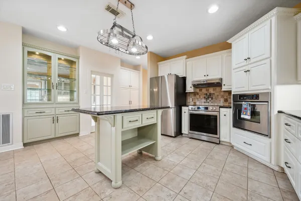 a kitchen with granite countertop a refrigerator oven a sink dishwasher and white cabinets with wooden floor