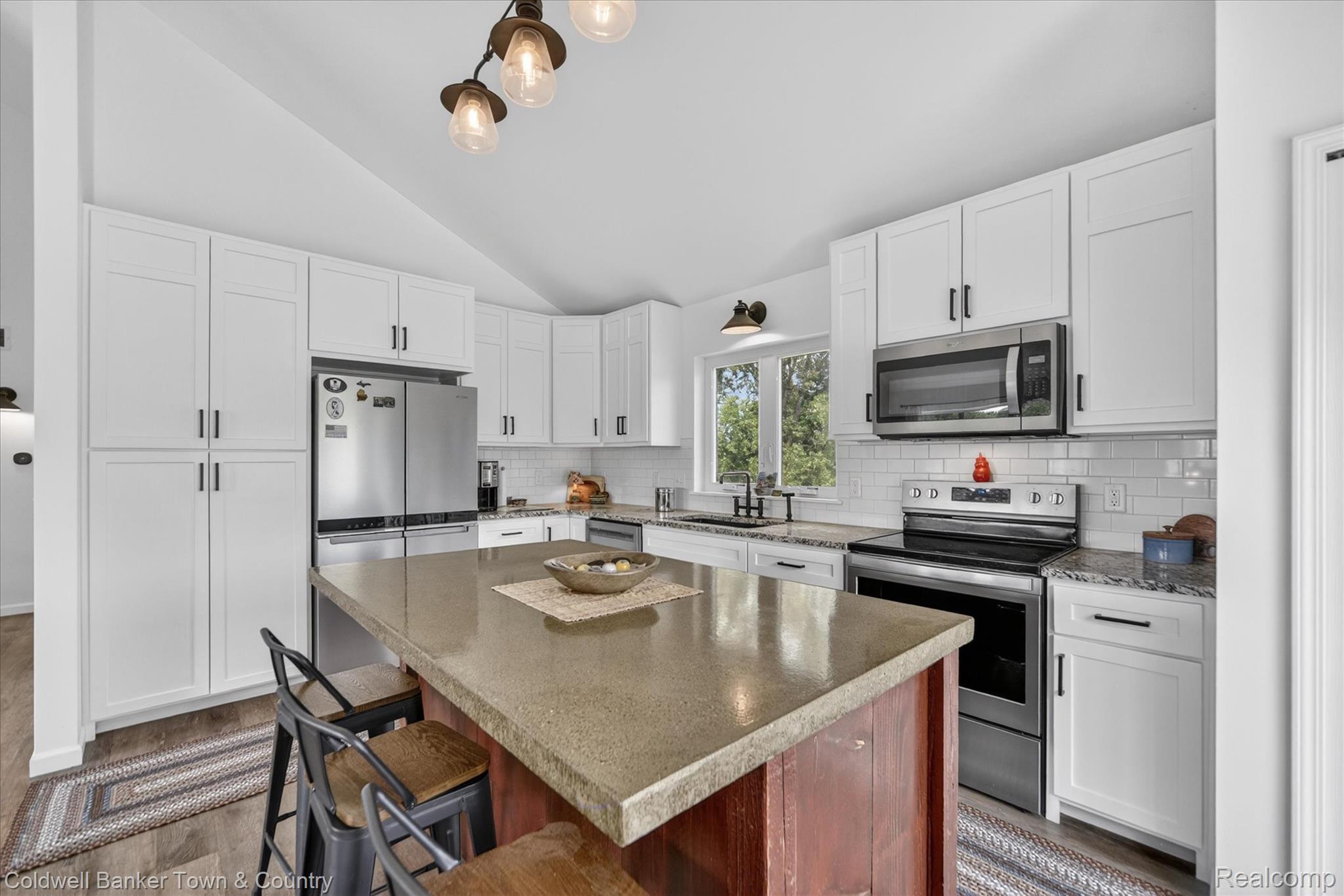 918 Gray Fox Court Howell, MI 48843 - Photo 51 of 84 Kitchen featuring a central island with a solid surface countertop, white shaker-style cabinetry, stainless steel appliances, a subway tile backsplash, and wood-finish flooring