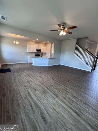 a view of an empty room with wooden floor and a ceiling fan