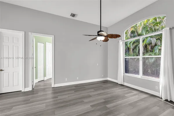 an empty room with wooden floor fan and windows
