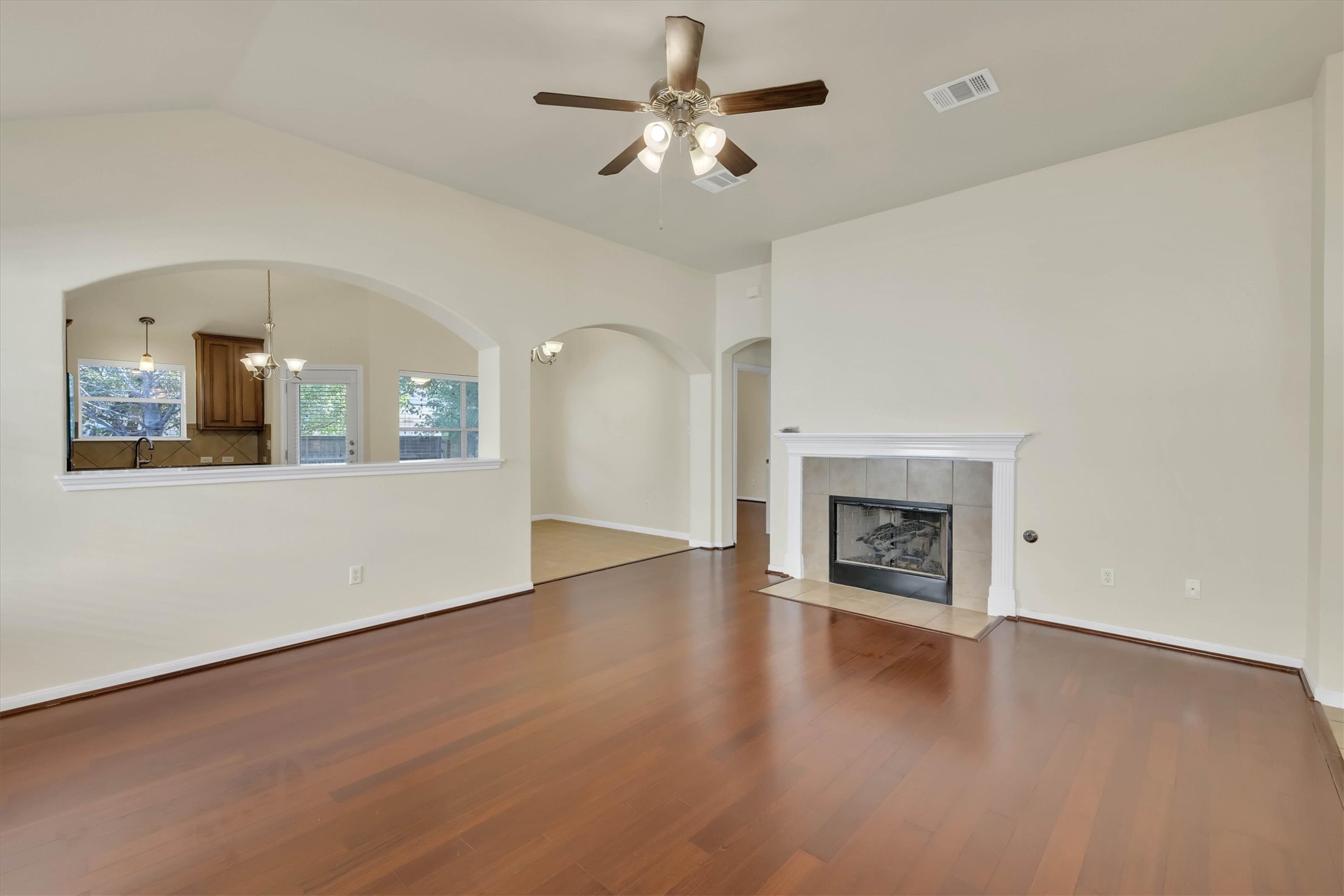 18420 Masi Loop Pflugerville, TX 78660 - Photo 5 of 33 Spacious living area featuring rich wood-finish flooring, a tiled fireplace with a classic mantle, vaulted ceilings, and an overhead ceiling fan
