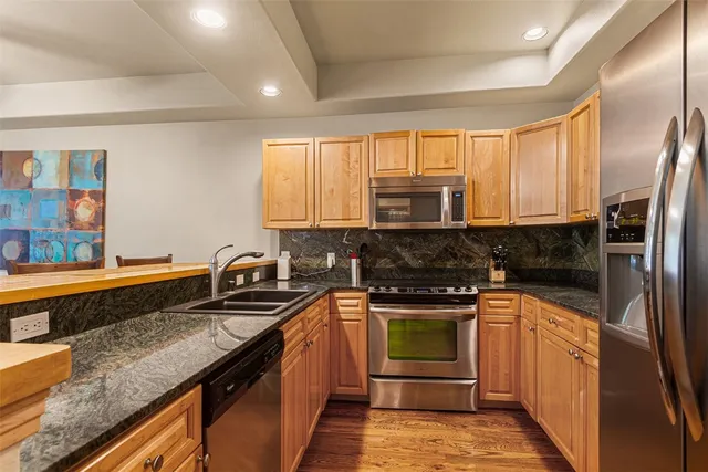 a kitchen with stainless steel appliances granite countertop a refrigerator a sink a stove a dining table and chairs with wooden floor