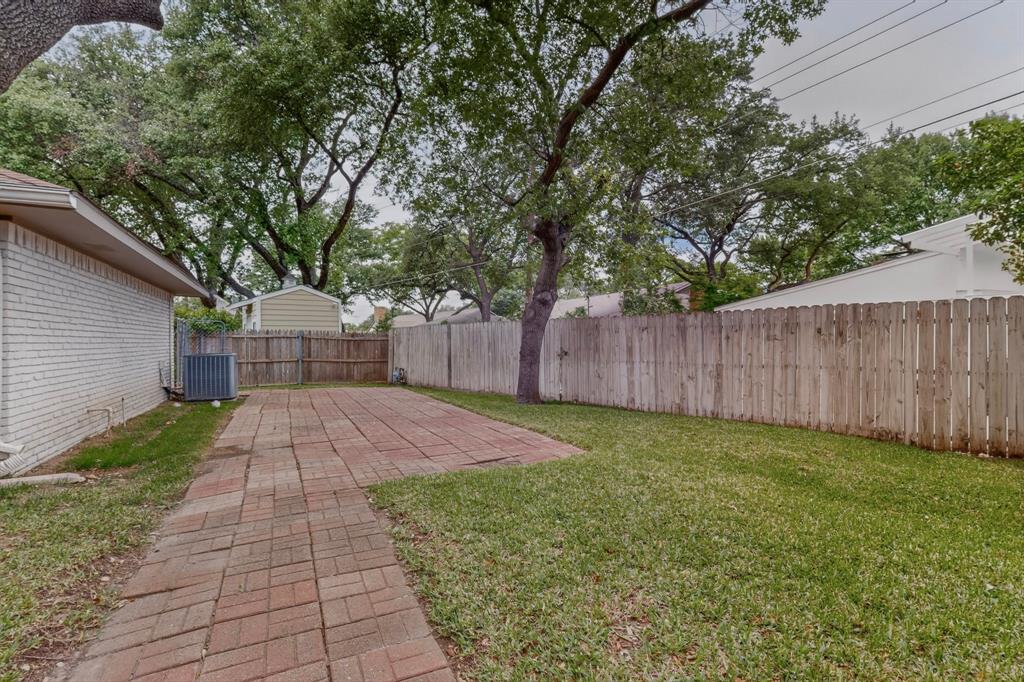 7631 Meadow Road Dallas, TX 75230 - Photo 35 of 40 A serene yard with a brick walkway surrounded by trees, inviting outdoor enjoyment.