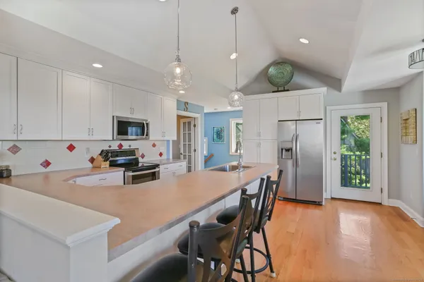 a kitchen with stainless steel appliances kitchen island granite countertop a refrigerator a stove a oven a sink a dining table and chairs with wooden floor