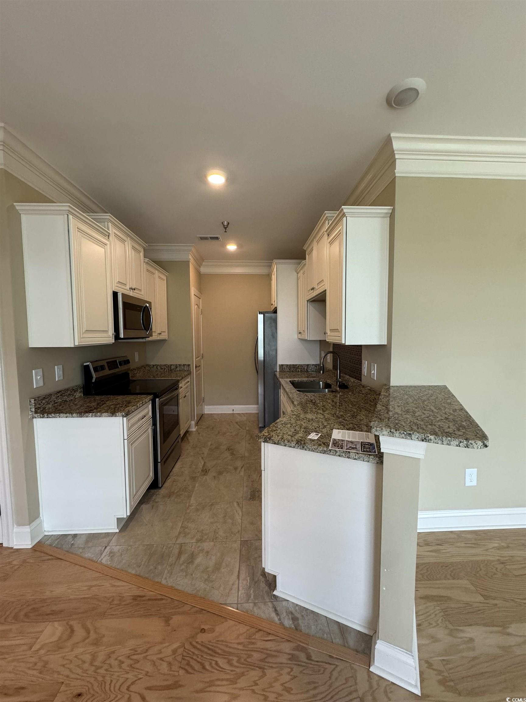 144 Puffin Drive, Unit 2E Pawleys Island, SC 29585 - Photo 9 of 17 Kitchen featuring stainless steel appliances, crown molding, dark stone countertops, a peninsula, and white cabinets