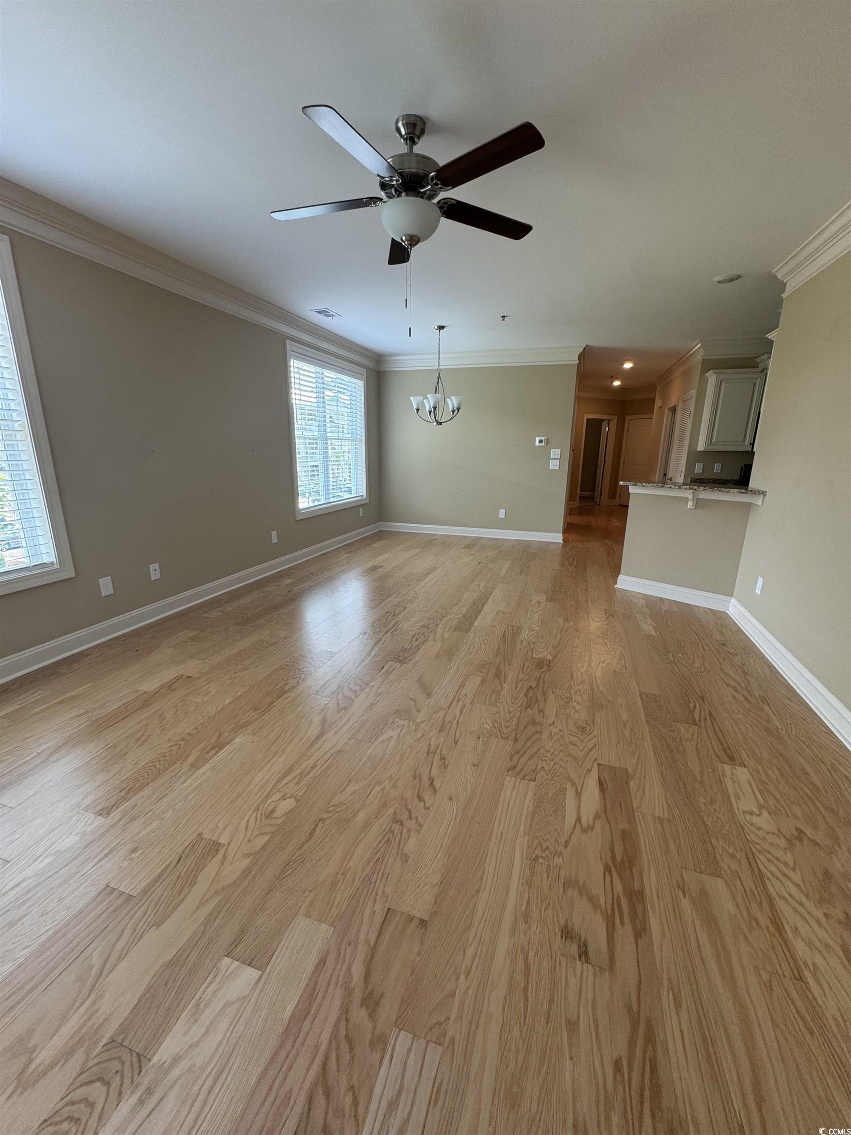 144 Puffin Drive, Unit 2E Pawleys Island, SC 29585 - Photo 10 of 17 Unfurnished living room with ornamental molding, a chandelier, light wood-style floors, and ceiling fan