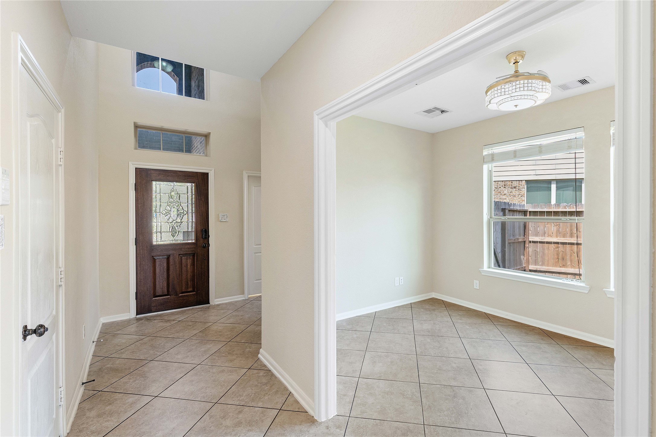 17206 Upper Ridge Lane Humble, TX 77346 - Photo 12 of 50 This photo showcases a bright entryway with a tiled floor and a decorative glass front door. Adjacent is a room with large windows, offering natural light and a view of the fenced yard, complemented by a modern light fixture.