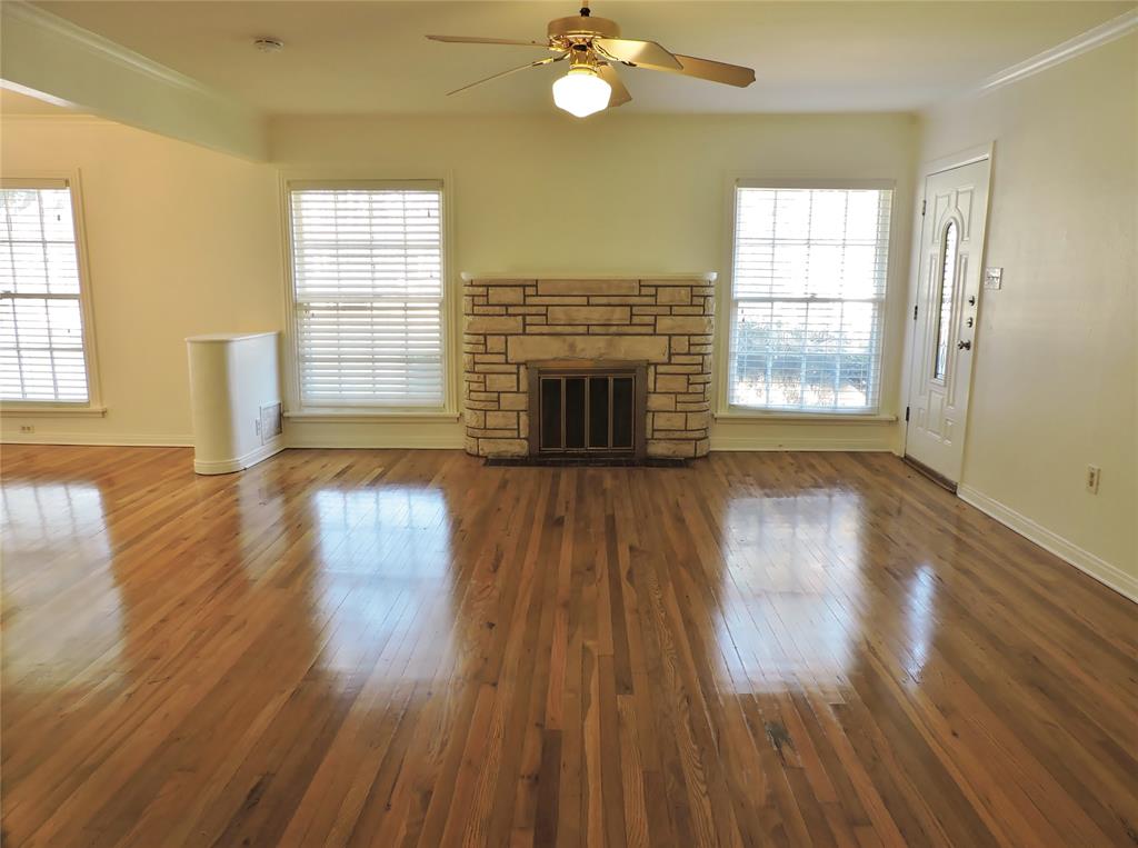 3425 Westcliff Road South Fort Worth, TX 76109 - Photo 2 of 22 Unfurnished living room featuring a stone fireplace, hardwood / wood-style flooring, a ceiling fan, and ornamental molding